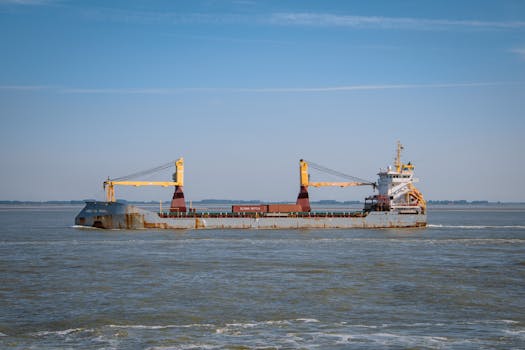 Cargo vessel carrying containers off the coast of Terneuzen in the Netherlands under a clear blue sky.