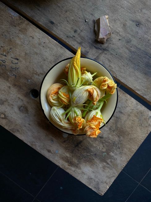 Top view of fresh squash blossoms in a bowl on a rustic wooden table.