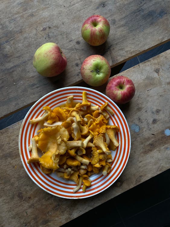 A Plate of Mushrooms Beside Red and Green Apples on a Wooden Table