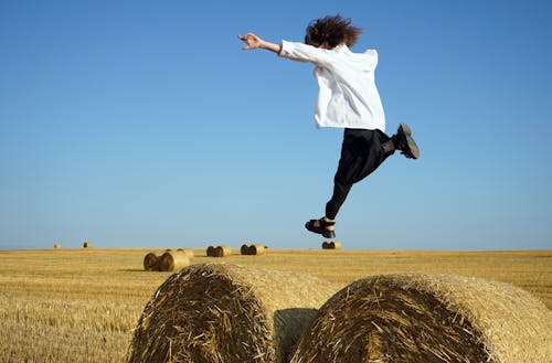 Man in White Long Sleeve Shirt and Black Pants Jumping on Brown Grass Field