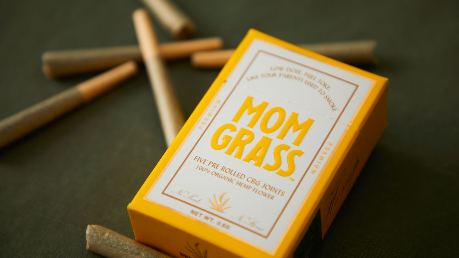 Close-up of Mom Grass CBG joints packaging with loose joints on a surface.