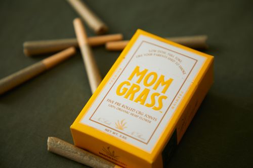 Free Close-up of Mom Grass CBG joints packaging with loose joints on a surface. Stock Photo