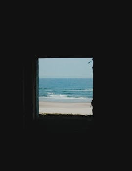 Serene ocean view framed by a dark room, showcasing seashore and waves.