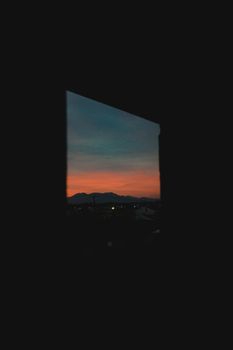 A dramatic view of silhouetted mountains and a colorful sunset framed by a window.