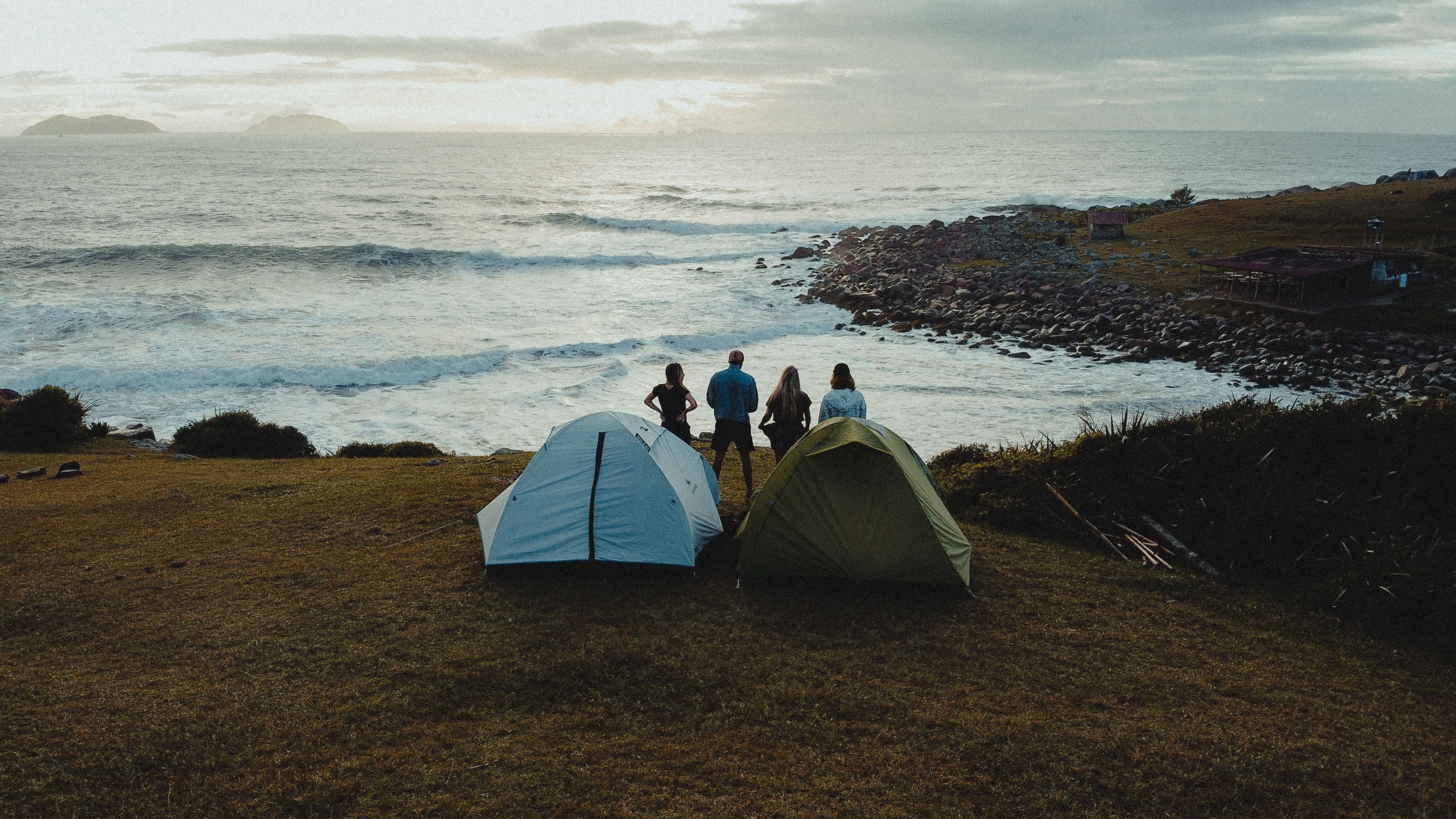 Group of campers relaxing on a tropical beach near the ocean at dusk