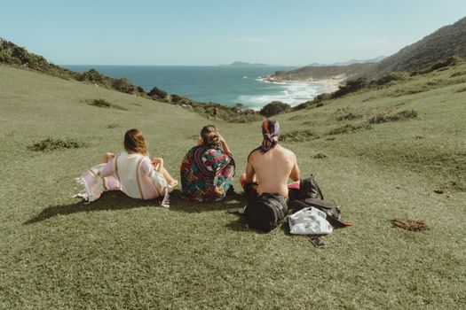 Three friends sit in tranquility, overlooking a stunning coastal landscape on a sunny day.
