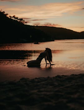 A woman poses gracefully on the beach during a stunning sunset.