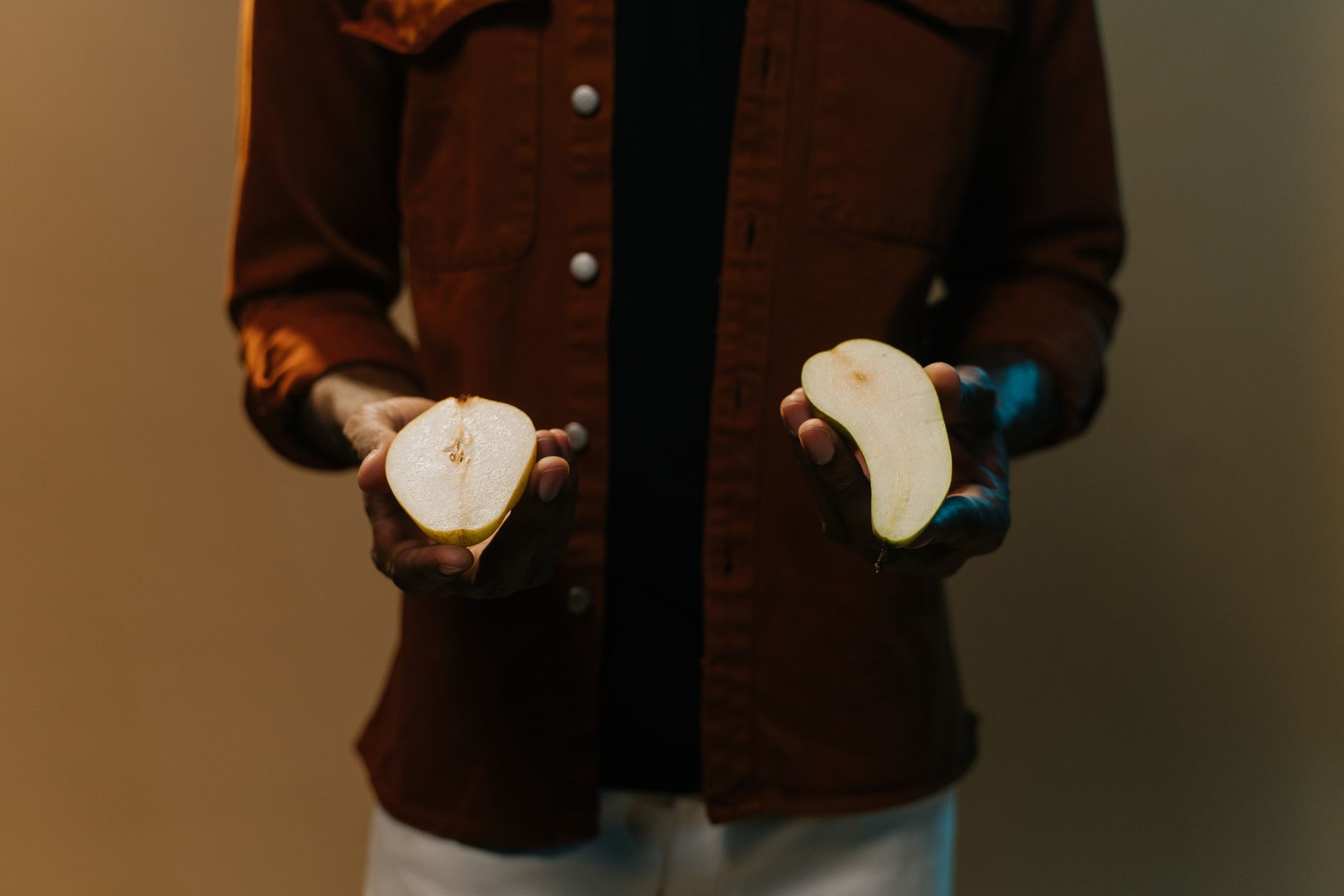 A person holding halves of a sliced pear in a studio setting, highlighting freshness.
