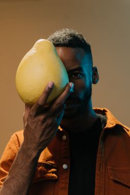 Homem segurando um pomelo inteiro na frente do rosto — mostrando o tamanho real da fruta