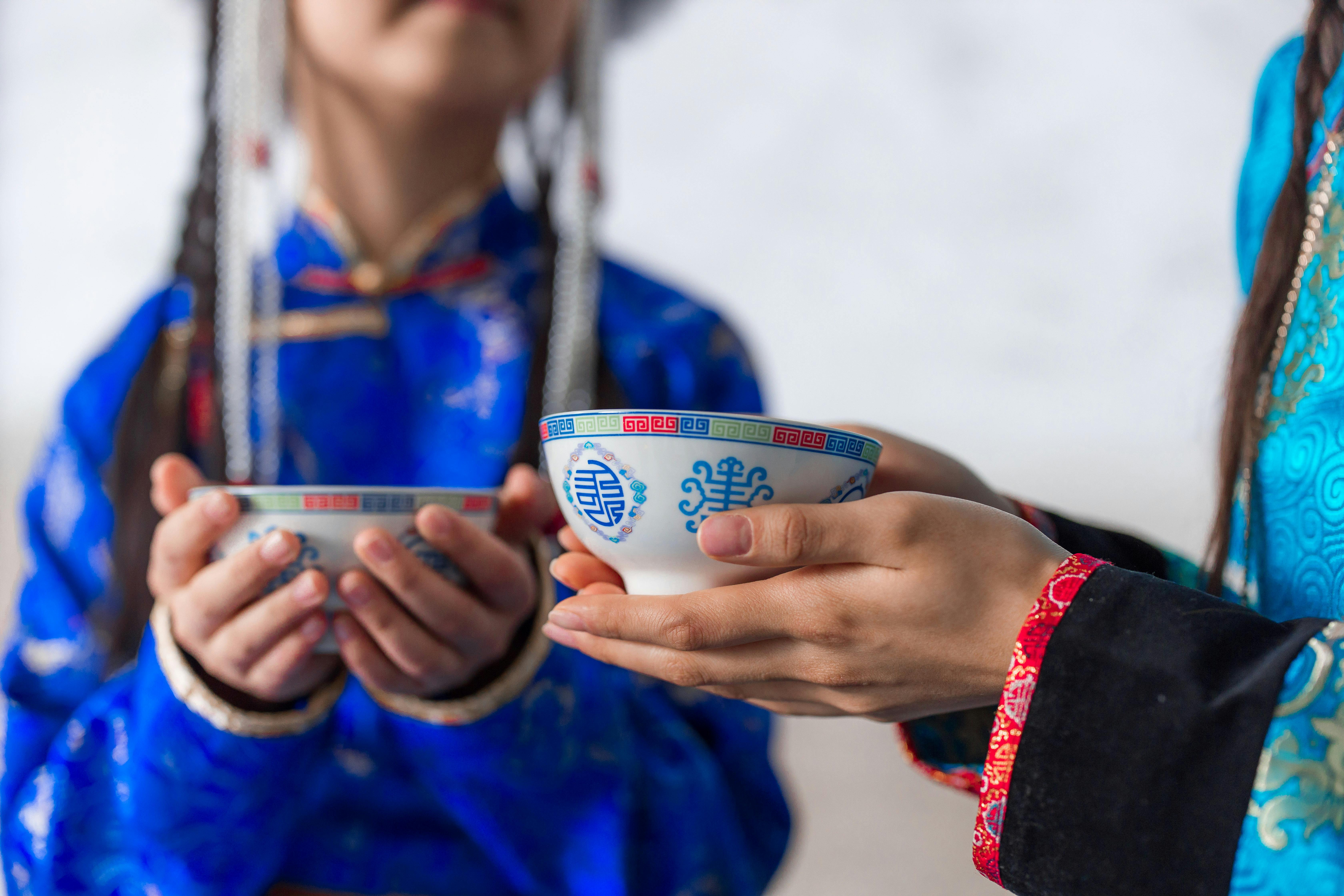 Close-up of people in traditional attire holding decorative tea cups during a ceremony indoors.