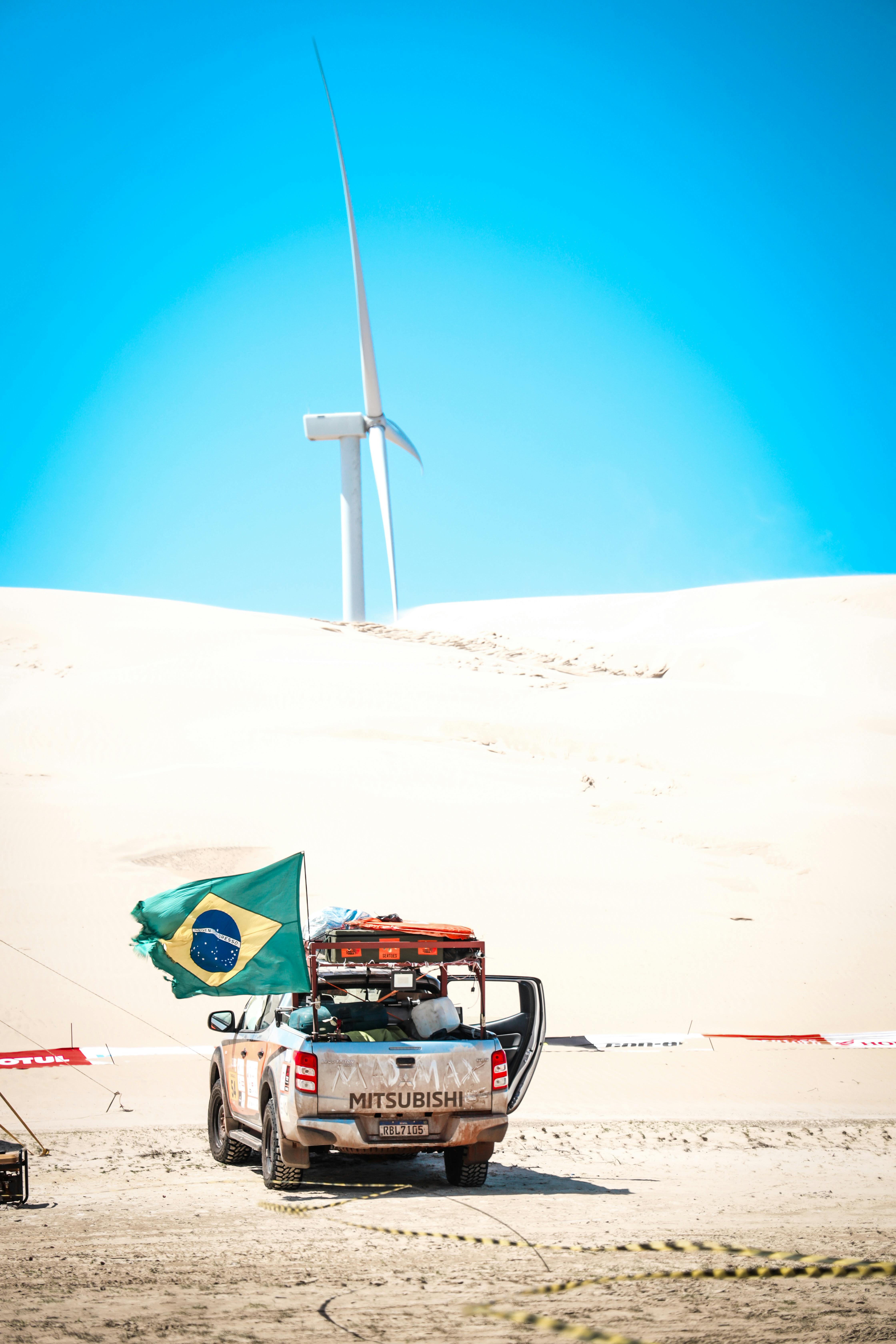 4x4 truck with Brazilian flag parked on sandy terrain with wind turbine in Barreirinhas, Brazil.