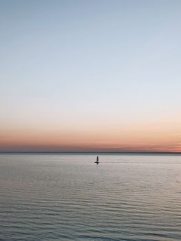 A tranquil scene of a lone sailboat on a calm sea at sunset, capturing serene nature beauty.