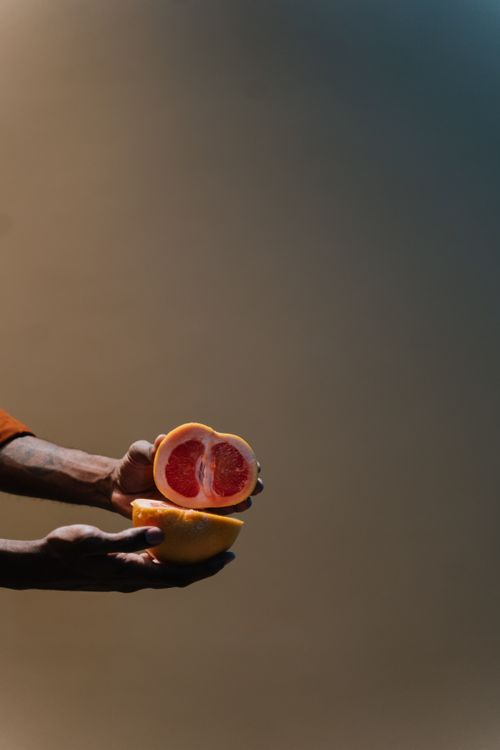 Free Artistic shot of hands holding a sliced grapefruit with neutral toned background, ideal for health and food concepts. Stock Photo