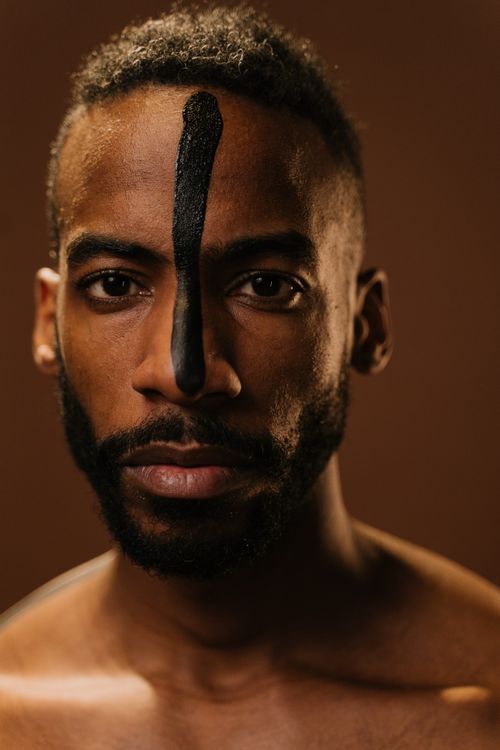 Free A striking portrait of a man with intricate face paint, captured in a studio with a warm brown background. Stock Photo