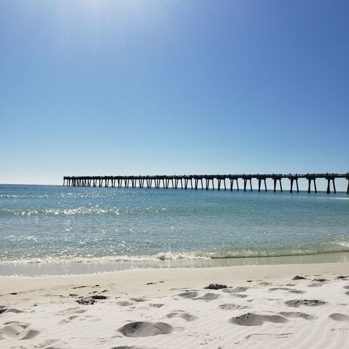 Free Serene beach view with an expansive ocean pier under a bright blue sky, perfect for relaxation. Stock Photo
