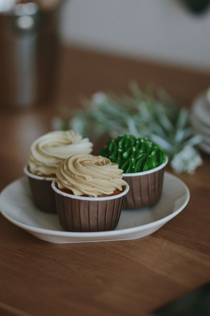 A dozen gluten-free vanilla cupcakes with swirled buttercream frosting on a marble countertop, one cupcake unwrapped from its paper liner in the foreground.