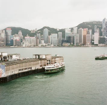 Scenic view of Hong Kong's Victoria Harbour with ferries and skyline of Kowloon and skyscrapers.