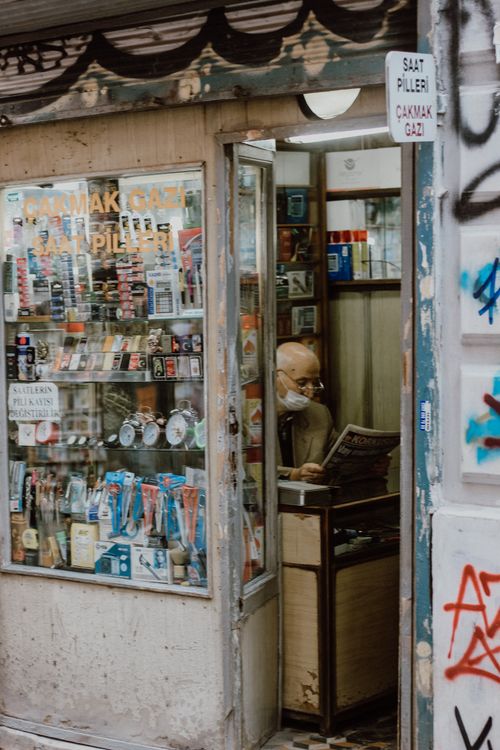 Free Senior man wearing mask reading newspaper in an eclectic store surrounded by various products and vintage decor. Stock Photo