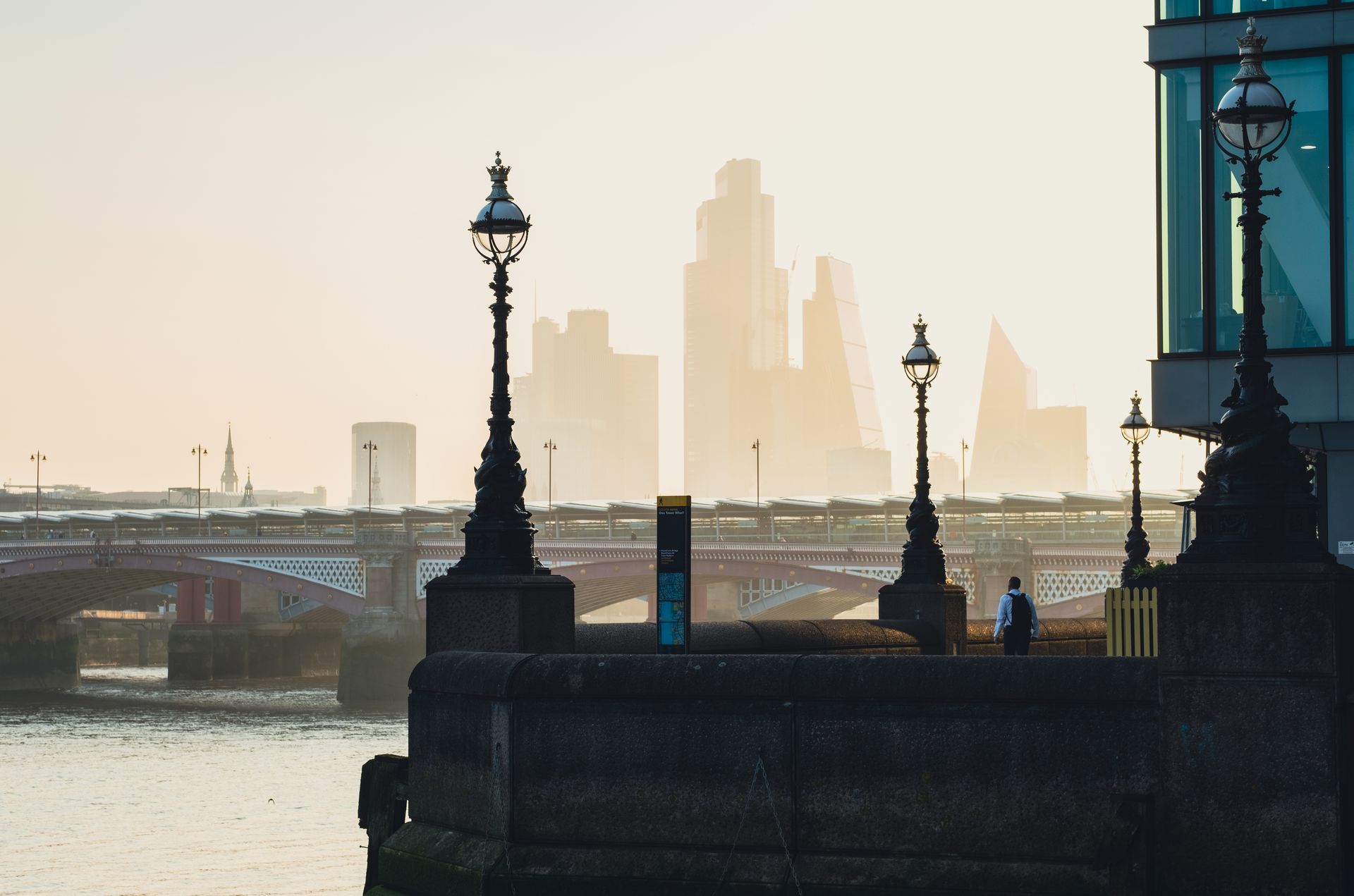 City skyline with river and bridge, featuring urban architecture and street lamps in foreground.