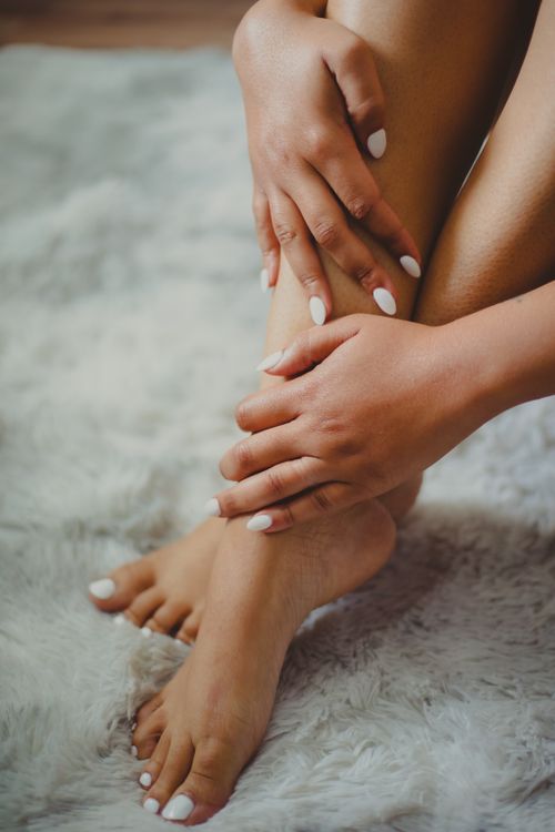 Free Aesthetic close-up of a woman's manicured hands and legs resting on a soft carpet. Stock Photo