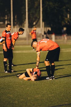 A soccer player lies injured on the field as teammates gather around in concern during a match.