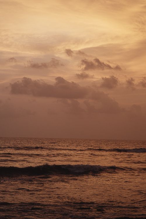 Free Captivating sunset with dramatic clouds and waves on the ocean horizon. Stock Photo