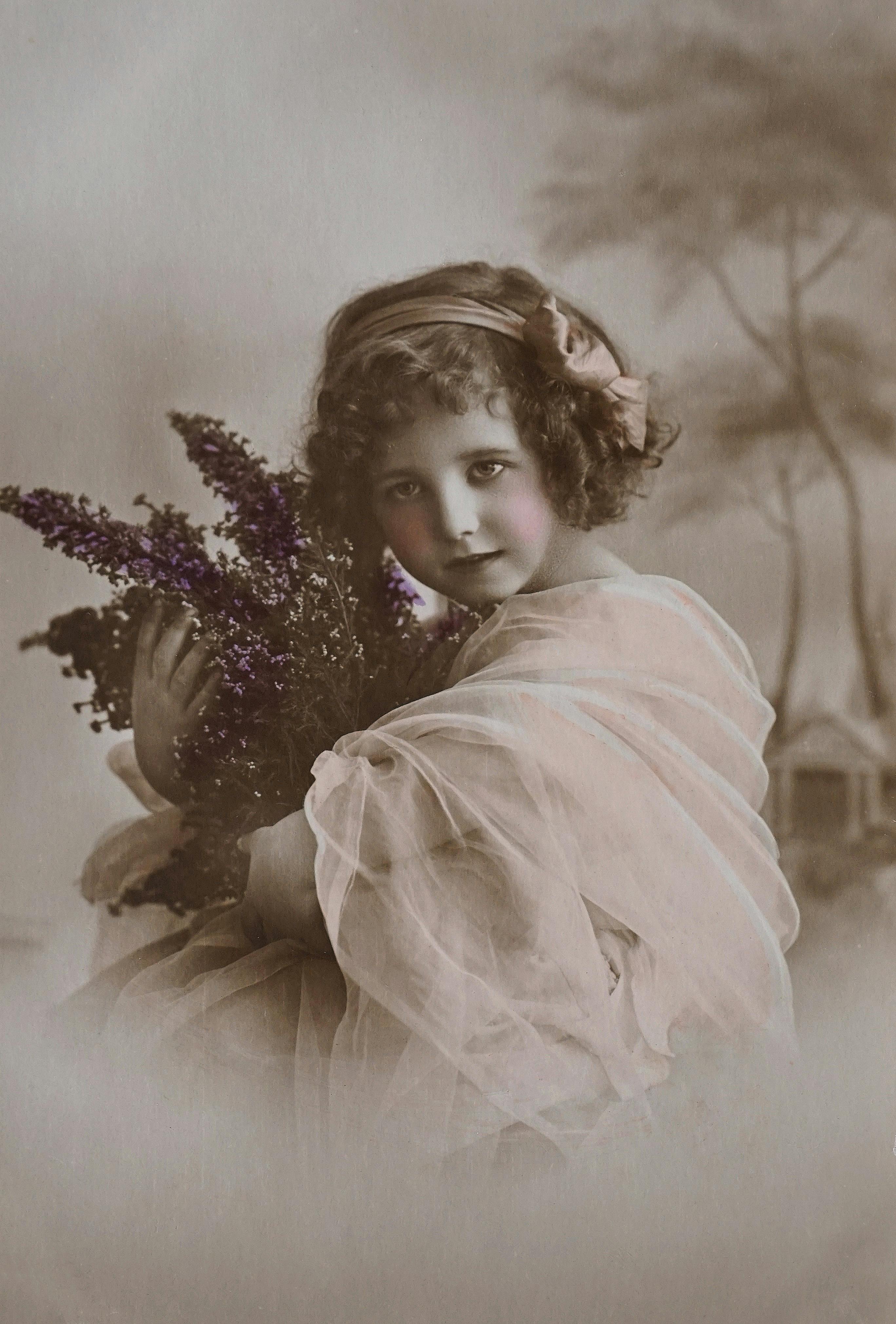 Sepia-toned vintage photo of a young girl holding a lavender bouquet, evoking nostalgic charm.