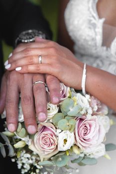 A close-up shot of newlyweds displaying wedding rings on their hands over a floral bouquet.