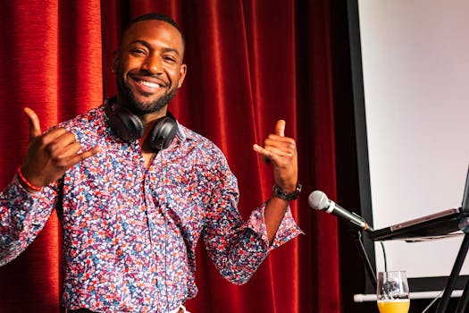 A cheerful DJ wearing a floral shirt and headphones poses indoors next to a microphone.