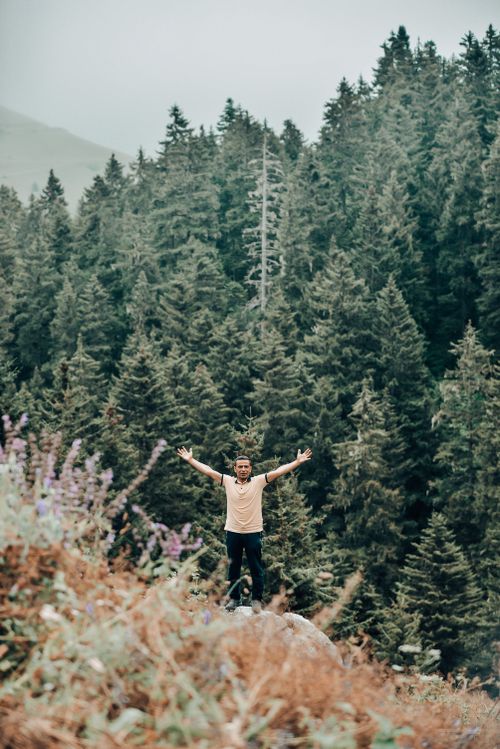 Free Man raising arms standing in dense forest, symbolizing freedom and adventure. Stock Photo