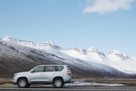 湛蓝的天空下，一辆银色越野车停在白雪皑皑的山前，展现出冬季的风景