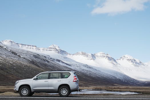 湛蓝的天空下，一辆银色越野车停在白雪皑皑的山前，展现出冬季的风景