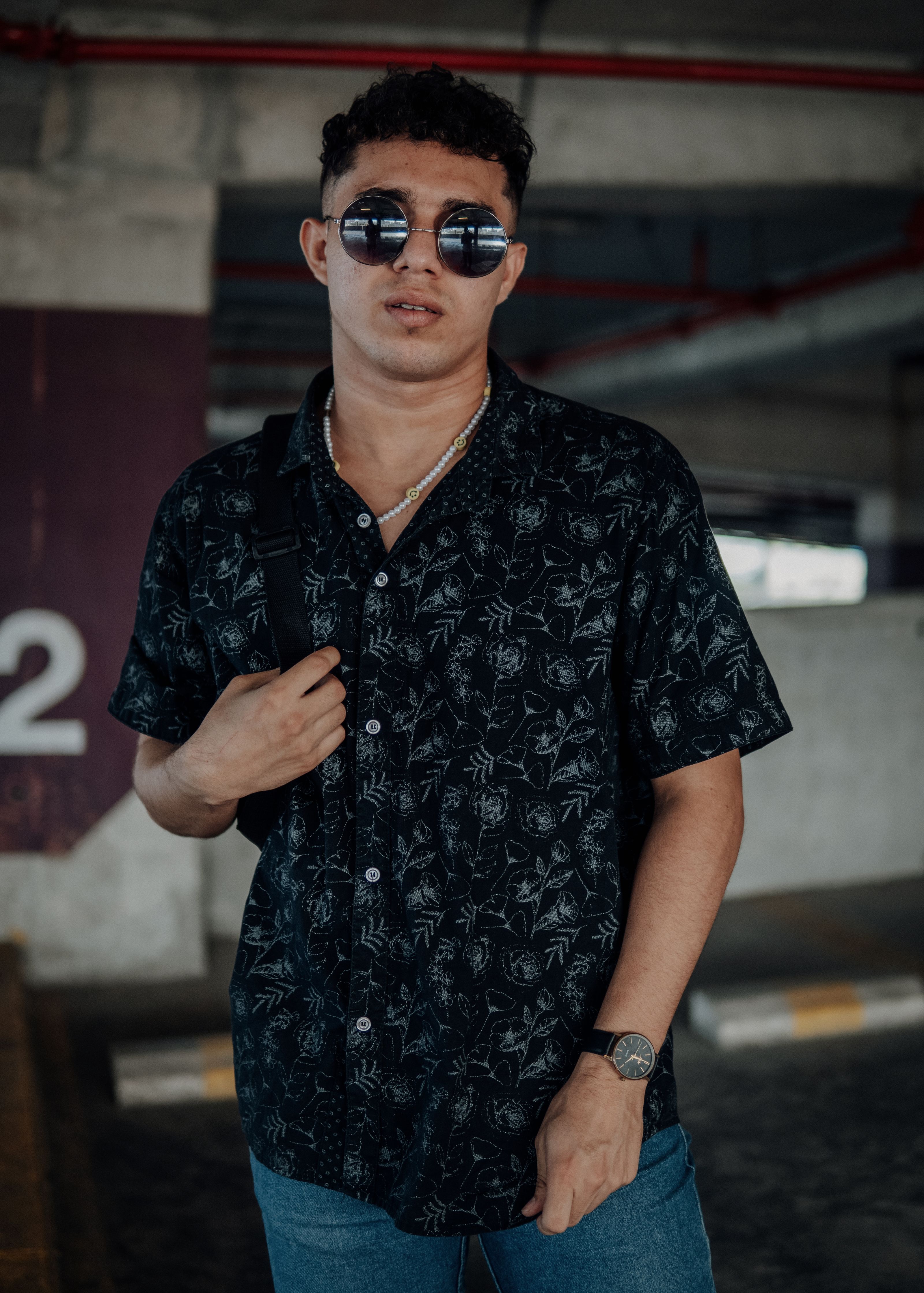 Um jovem da moda posando com confiança em um traje urbano, com óculos de sol estilosos em uma garagem.
