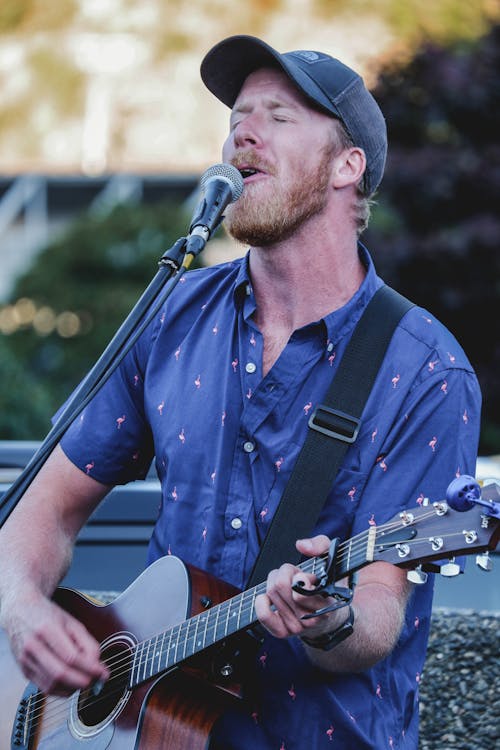 Selective Focus Photo of a Performer Singing and Playing the Guitar