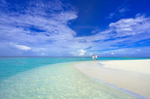 Free A serene beach scene with a couple walking along the turquoise shoreline under clear blue skies. Stock Photo