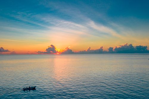 Free A serene sunset over the ocean in Fuvahmulah, Maldives with a boat in the foreground. Stock Photo