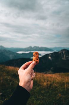 A hand holding a cookie with a scenic mountain range in the background, creating a unique outdoor food scene.