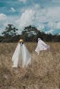 Woman in White Wedding Dress Standing on Brown Grass Field