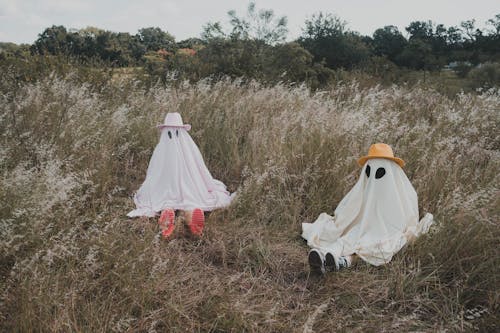 Two People in White Spooky Costumes Sitting on Grass Field