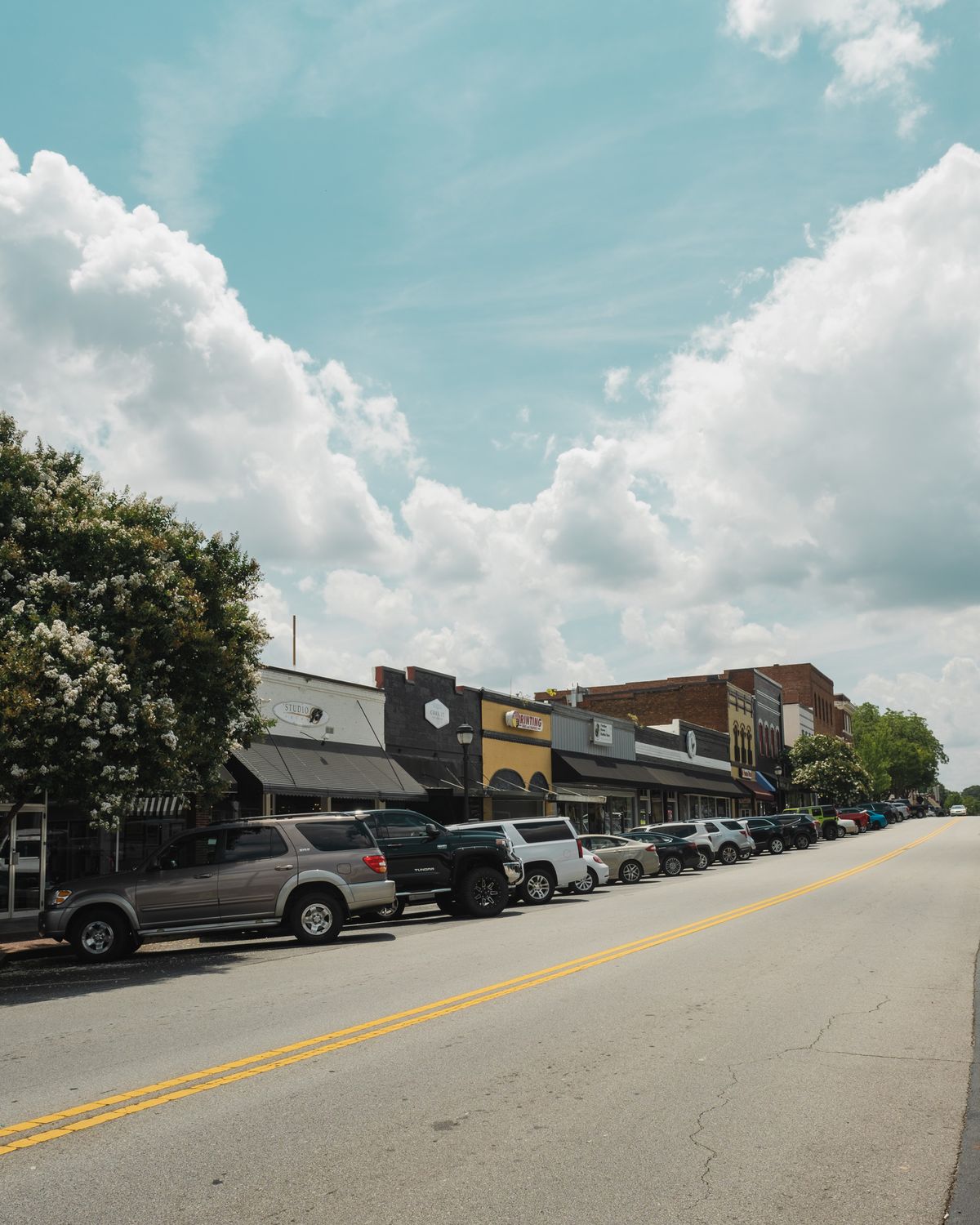 A vibrant main street in Buford, Georgia with parked cars and quaint storefronts under a cloudy sky. Illustrative editorial photograph.