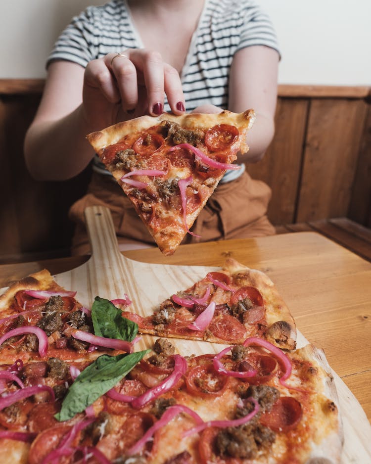 A Woman Holding A Slice Of Thin Crust Pepperoni Pizza  