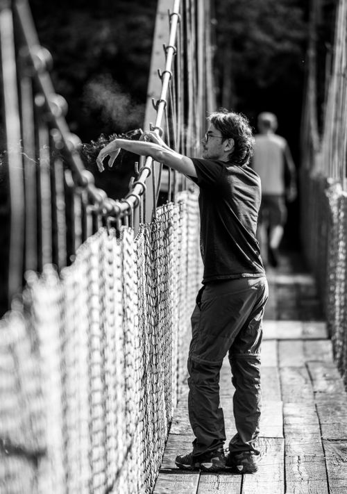 Free Black and white photo of a man on a suspension bridge, capturing a reflective moment. Stock Photo