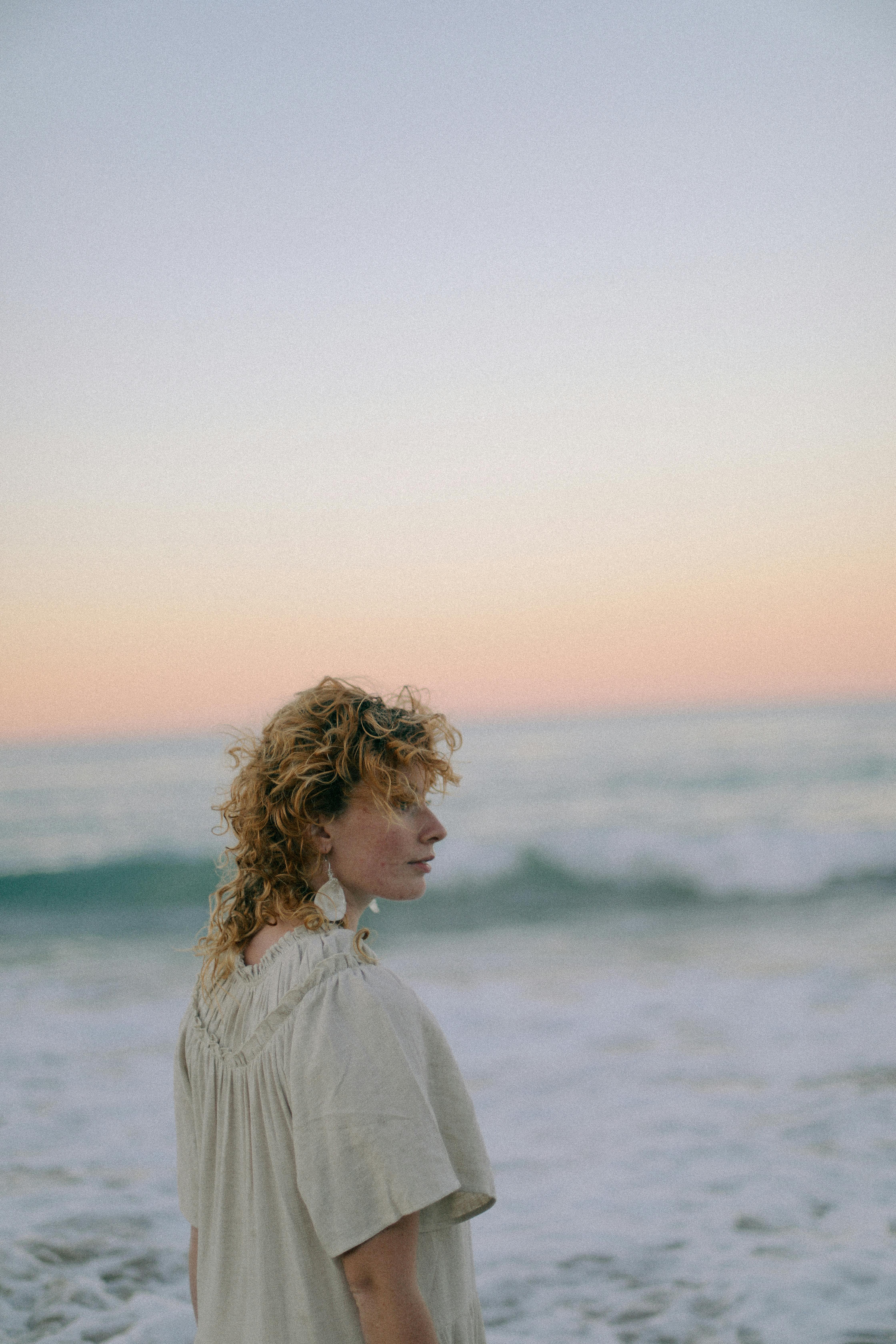 A contemplative woman gazes at the ocean during a tranquil beach sunset.