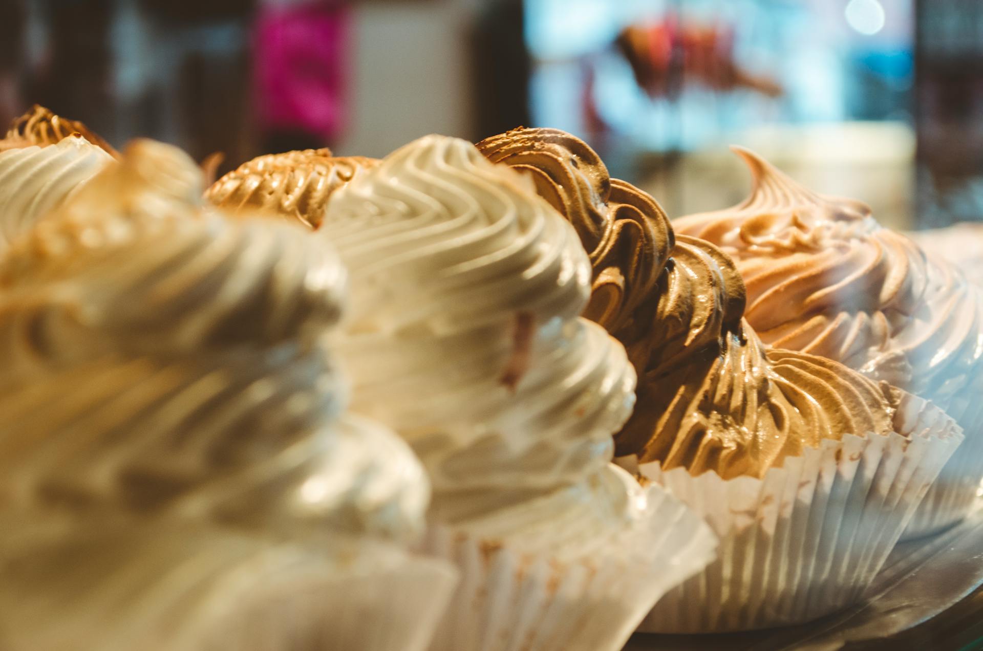 Close-up of various cupcakes with swirled frosting on display in a bakery.