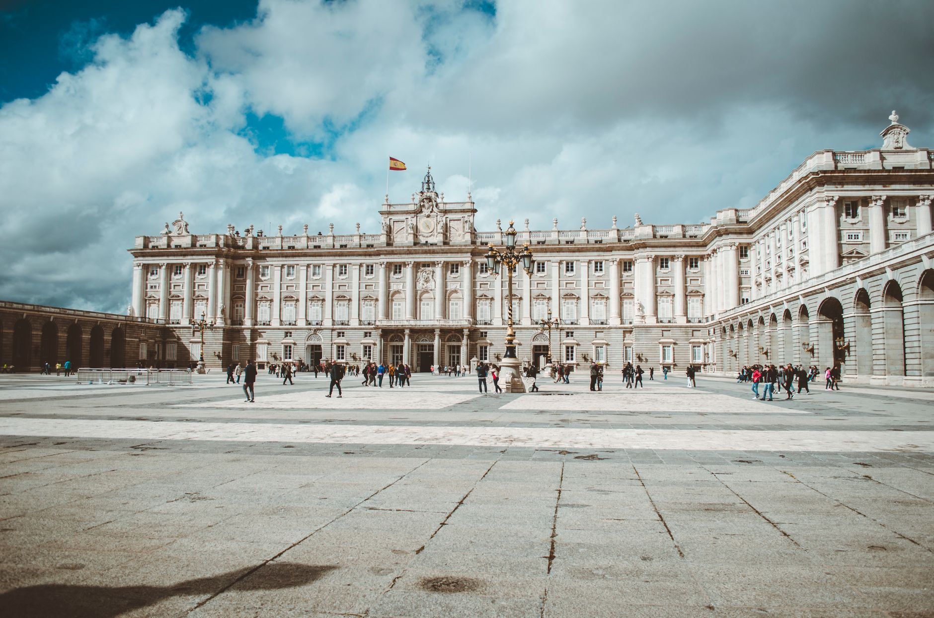The majestic Royal Palace of Madrid with tourists enjoying a cloudy yet beautiful day.