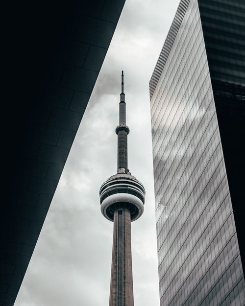 Free Low-angle view of the iconic CN Tower framed by skyscrapers in Toronto under a cloudy sky. Stock Photo