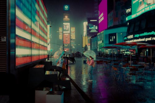 Free People Standing on the Street while Raining at Night Near the Buildings with Digital Billboards Stock Photo