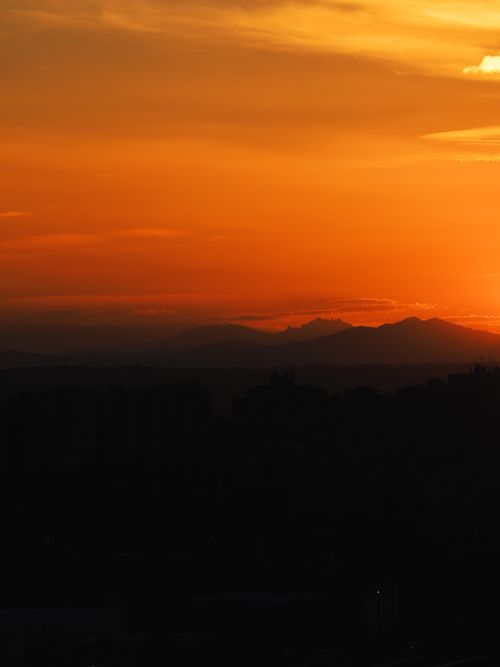Free A breathtaking view of a sunset casting silhouettes over distant mountains and a vibrant sky. Stock Photo