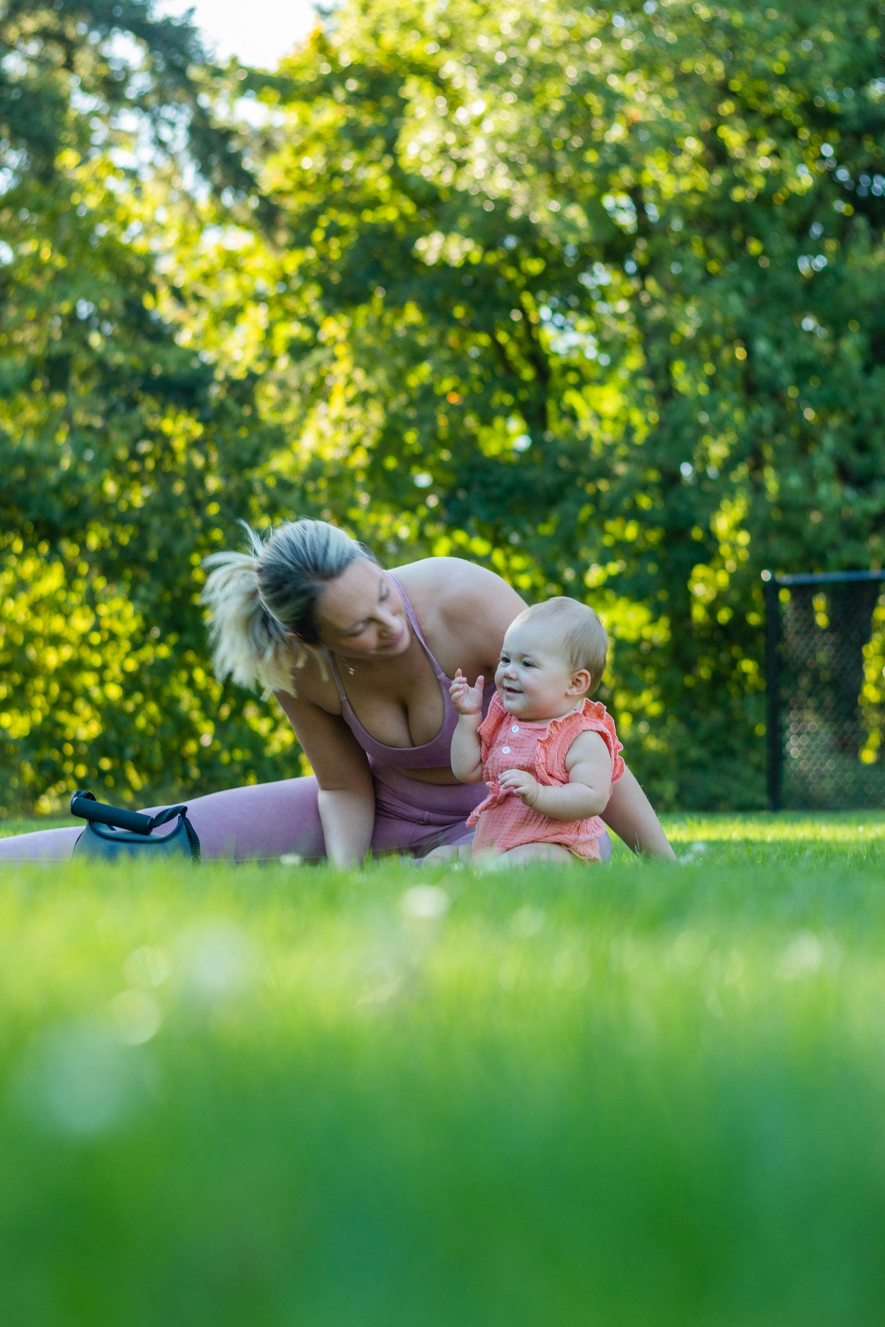 a woman sitting on green grass with her baby girl