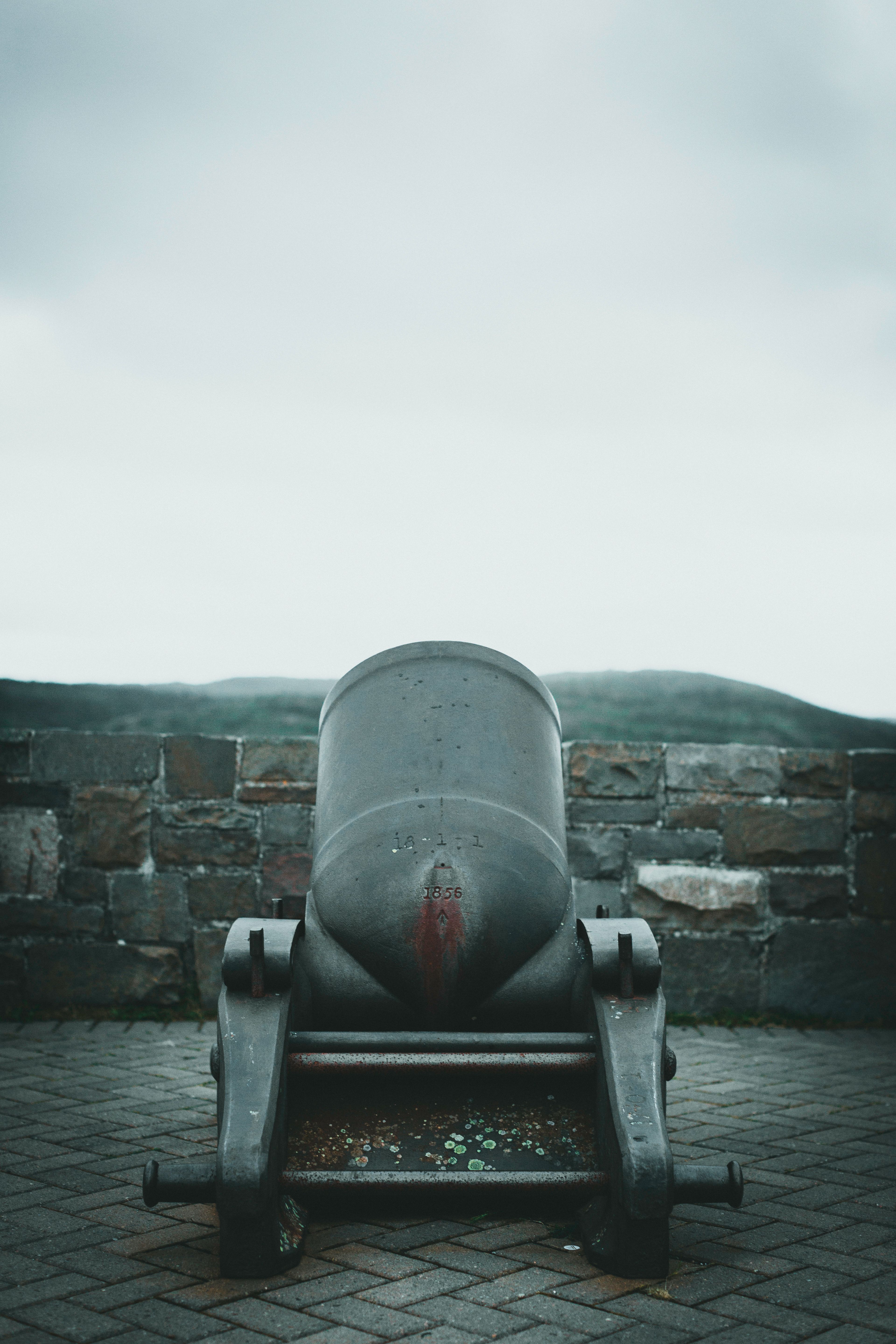 Rusty vintage cannon on a brick floor with a backdrop of a stone wall under a cloudy sky.
